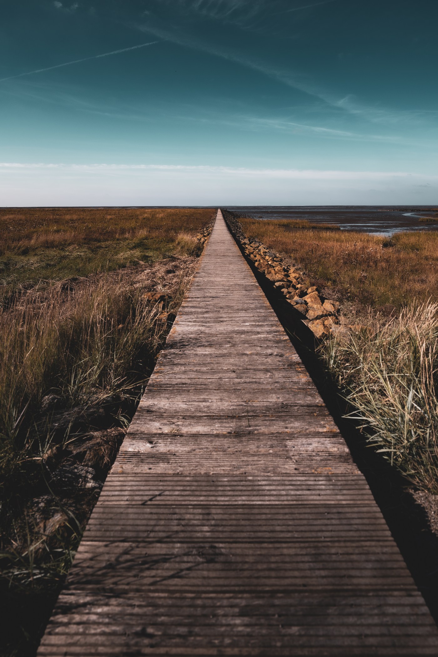 Langer Holzsteg entlang der Marschlandschaft, der direkt in die Nordsee führt